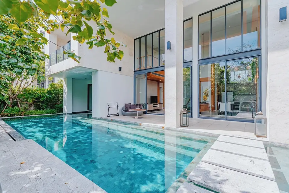 Villa med høje glaspartier, overdækket terrasse og pool langs facaden.
