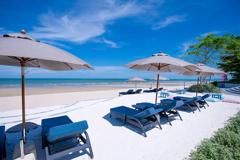 Loungestole og parasoller på sandstrand ved Baba Beach Club i Hua Hin med roligt hav og blå himmel.