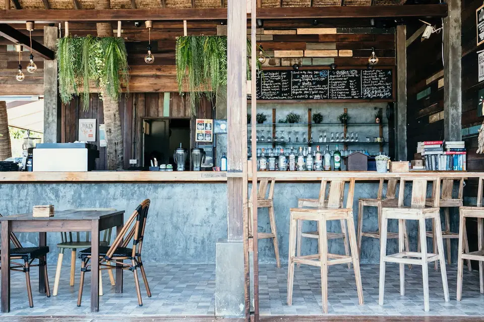 Hyggelig, moderne café med træmøbler og grønne planter langs loftet, stemning af afslappet strandliv på baren i Beach Loft-stil.