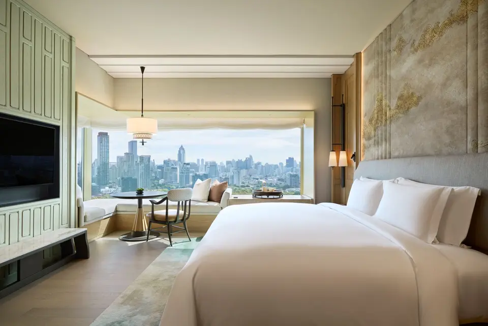 Elegant hotelværelse i Bangkok med stor seng, siddeområde og panoramaudsigt over byens oplyste skyline.