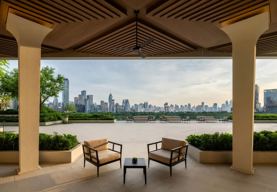 To terrassestole og et lille bord på Dusit Thani Bangkoks overdækkede terrasse med udsigt til byens skyline og frodig patio.