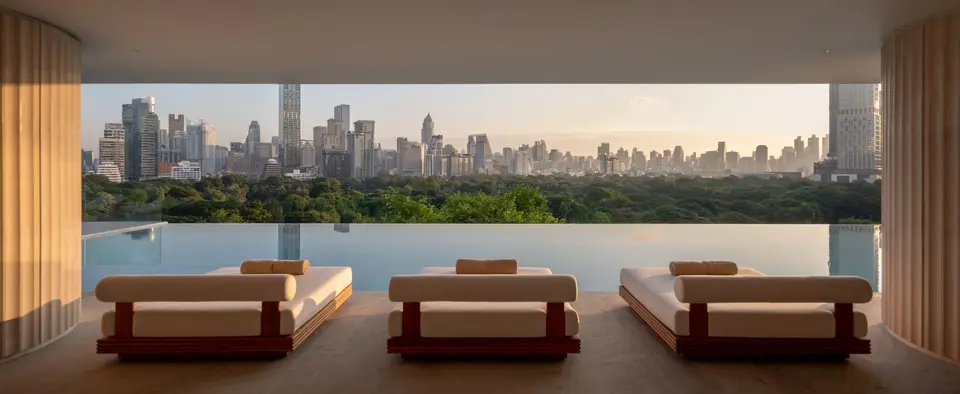 Moderne loungestole ved infinity-pool på Dusit Thani Bangkok med udsigt til solnedgang over byens skyline og grøn park.