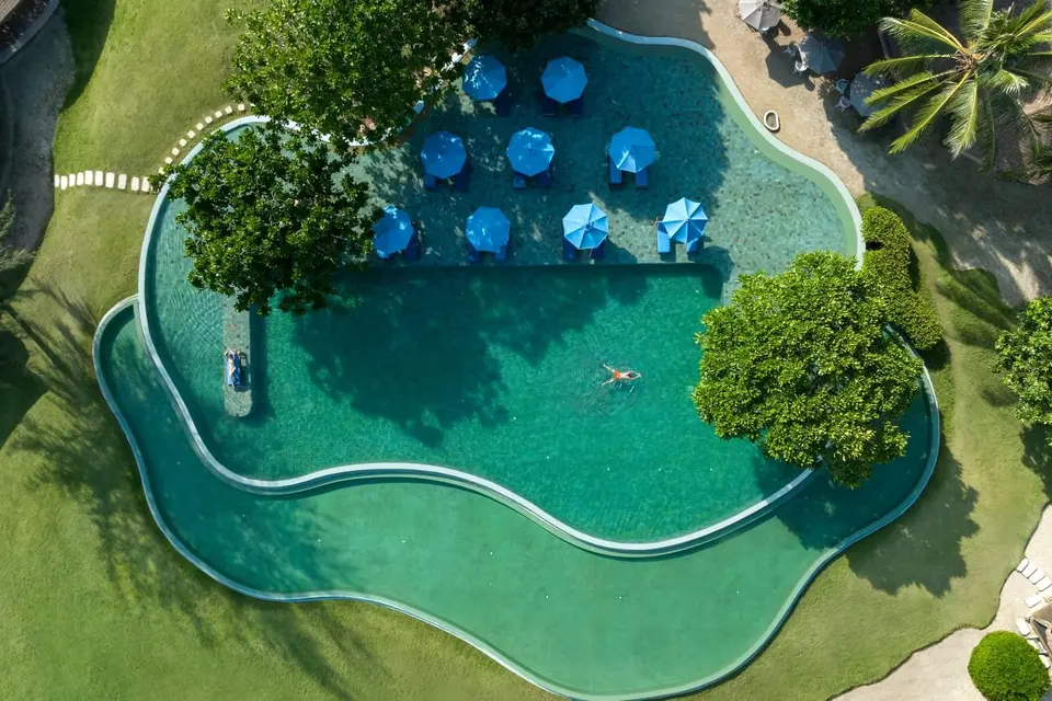 Pool med runde terrasser og blå parasoller set ovenfra