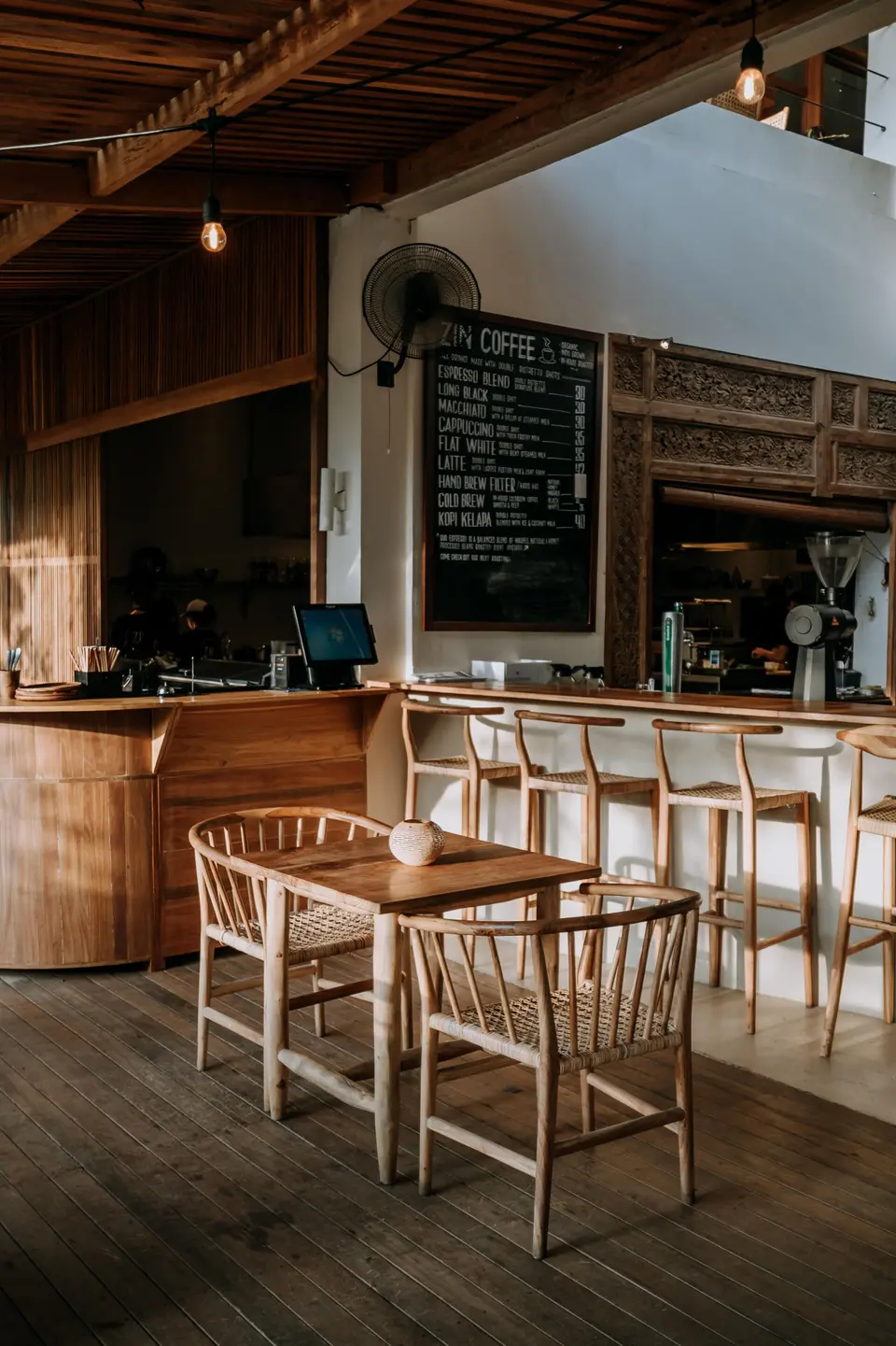 Café på ZIN Canggu med træborde, stole og bardisk under et træloft.