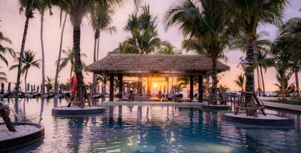 Solnedgangsudsigt over swimmingpool med omgivende palmer på La Flora Resort i Khao Lak